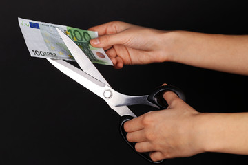 Poster - Hands with scissors cutting Euro banknote, on black background