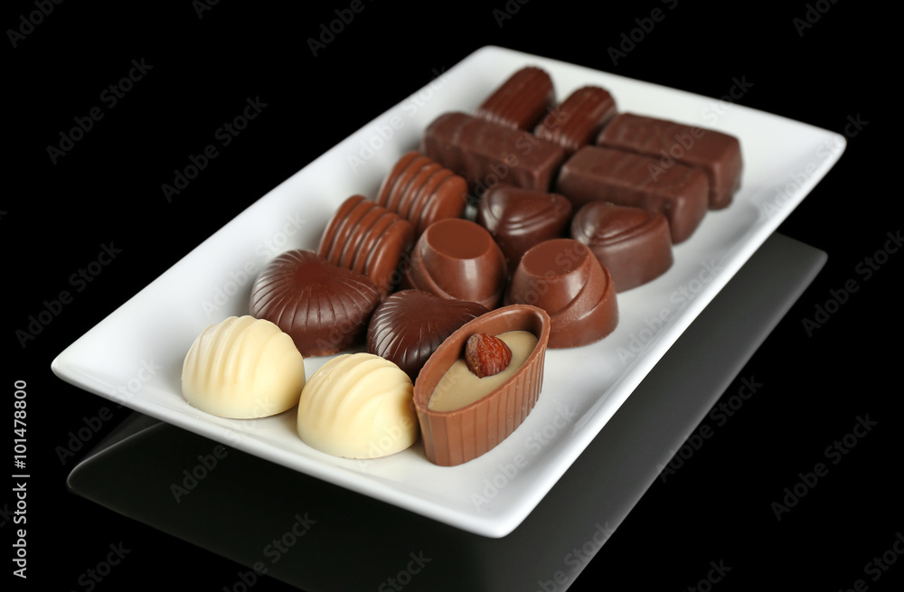 Assorted chocolate candies on white plate over black background