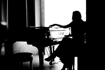 black and white woman silhouette sitting near piano