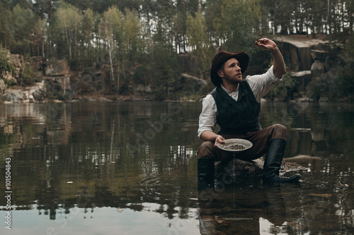 Fotografia, Obraz unshaved golddigger washes gold in the lake with rocky bank