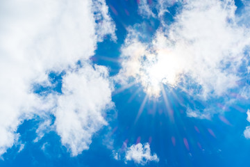 looking up at sun ray behind cloud with light flare and blue sky