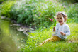 © Suzi Media  - Sweet, happy little girl sitting on a grass in a park at a spring stream with flower in hand. Laughing, enjoying fresh air in forrest.