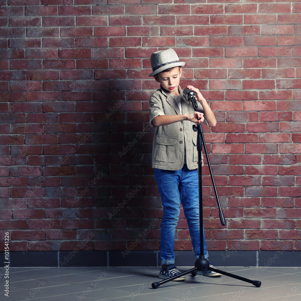 Little boy singing with microphone on a brick wall background