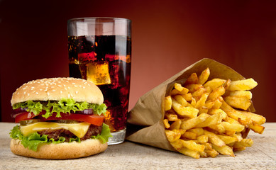 Cheeseburger with drink of cola and french fries on red spotlight