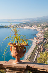 Wall Mural - View of an ornamental vase in a panoramic balcony of the public garden in Taomina with the touristic village Giardini Naxos in the background