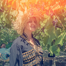Portrait Of Woman Wearing Traditional Felt Cloak And Fur Cap Outdoor In The Grape Garden