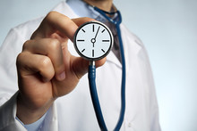 Male Doctor Holding Stethoscope With Clock