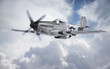 World War II era fighter flies among clouds and blue sky