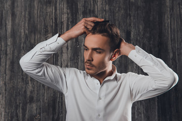 Wall Mural - Attractive rigid man combing hair on the grey background