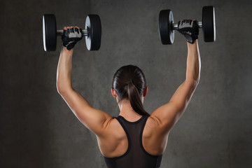 Poster - young woman flexing muscles with dumbbells in gym