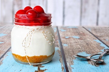 Sweet cherry cheesecake in a mason jar on a rustic wood background