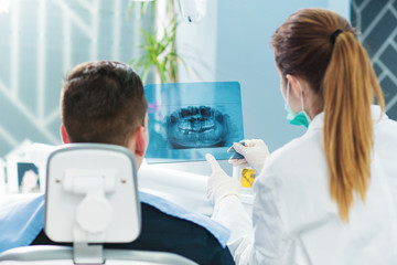 Dentist showing to patient roentgen of human jaw and giving him an advice. Shallow depth of field.