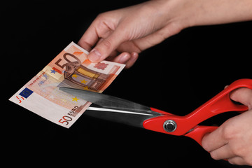 Poster - Hands with scissors cutting Euro banknote, on black background