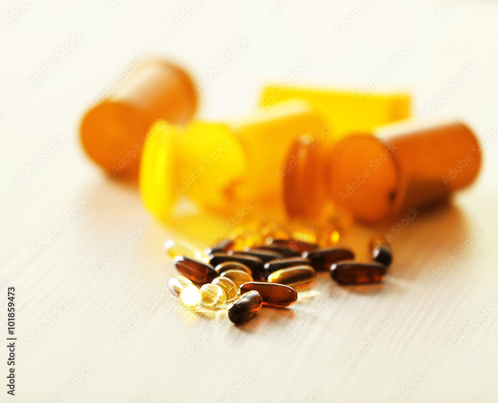 Different capsules spilled from orange pill bottles on wooden table, close up