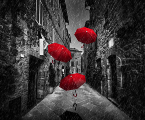 Fototapete - Umrbellas flying with wind and rain on dark street in an old Italian town in Tuscany, Italy
