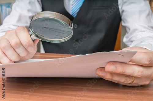Fotografie, Obraz Businessman is inspecting contract with magnifying glass.