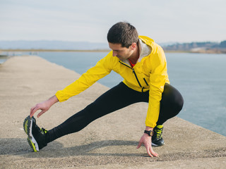 Male runner stretching on a river dock