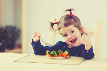 Wall Mural - happy child girl loves to eat vegetables and showing thumbs up