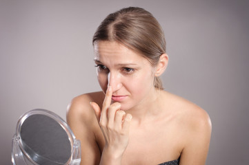 Young woman checks her nose in the mirror