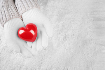 Poster - Hands in warm white gloves holding red heart on snowy background