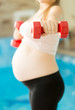 Closeup of young pregnant woman lifting dumbbell at gym