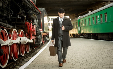 man in retro suit with suitcase walking on the train platform