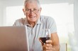 © WavebreakmediaMicro - Focused senior man using laptop and drinking wine