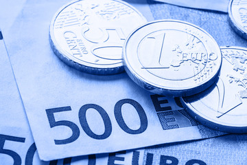 Several 500 euro banknotes and coins are adjacent. Symbolic photo for wealt.Euro coin balancing on stack with background of banknotes.