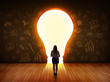 © ra2 studio - Business woman looking at bright light bulb in the wall