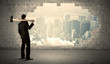 © ra2 studio - Business man hitting wall with hammer on city view
