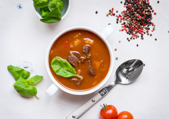 Tomato soup with meat in a white bowl on a white wooden backgrou