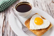 Fried egg on bread for breakfast on plate with a cup of coffee and rustic table