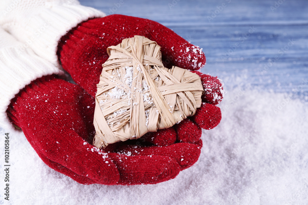 Female hands in mittens with decorative heart on snow background