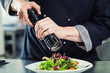 Chef Koch in Restaurant würzt Salat mit Pfeffer aus Pfeffermühle
