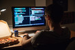 © Drobot Dean - Back view of focused programmer writing code and eating pizza
