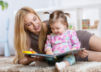 sweet baby girl with mother reading book in nursery