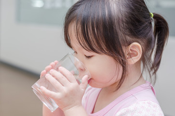 Little Asian girl drinking water from glass