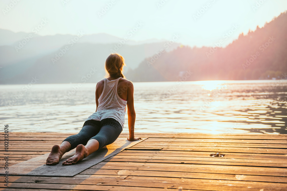 Yoga sun salute. Young woman doing yoga by the lake at sunset - obrazy, fototapety, plakaty 