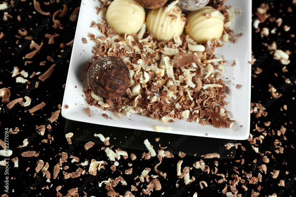 Assorted chocolate candies on white plate with flakes over black background