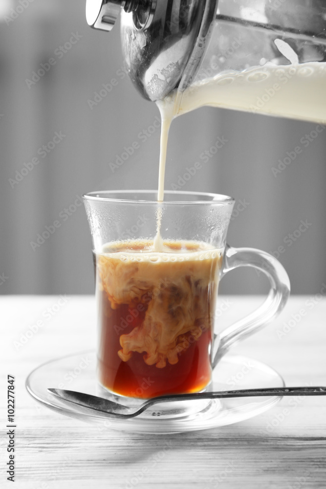 Pouring milk in coffee on light wooden table