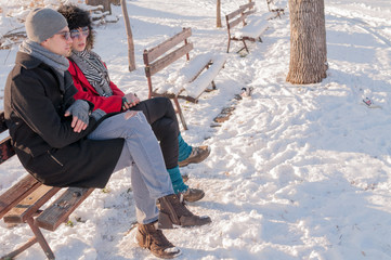 Young couple sitting on bench in park in winter and talking