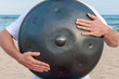Busker on the sand beach and holding a handpan or hang with sea On Background. The Hang is traditional ethnic drum musical instrument