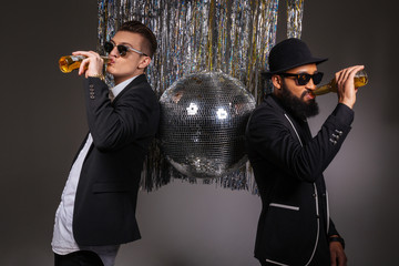 Wall Mural - Two confident men standing near disco ball and drinking beer