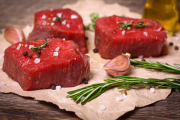 Raw beef steak with rosemary, thyme and garlic on wooden background