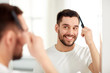 © Syda Productions - happy man brushing hair  with comb at bathroom