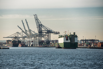 cargo ship sailing to commercial port with cranes for unload