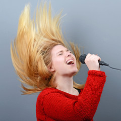 Beautiful woman singing with the microphone against gray backgro