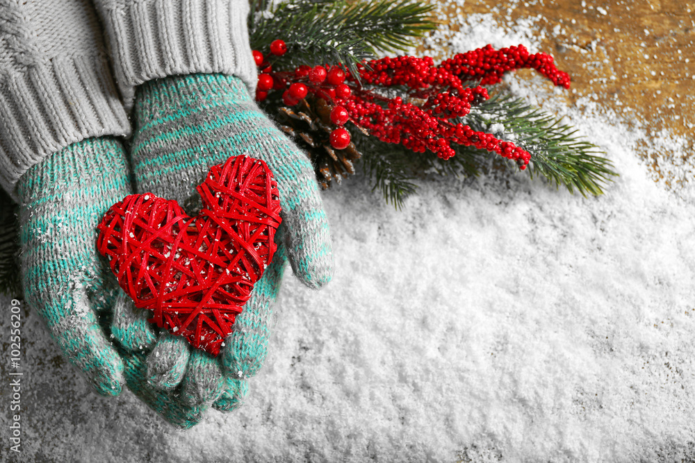 Female hands in blue mittens with decorative heart on snow background