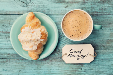 Wall Mural - Coffee mug with croissant and notes good morning on turquoise rustic table from above, cozy and tasty breakfast, vintage toned