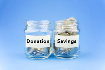 Two glass jars with coins labeled Donation and Savings on blue background. Financial Conceptual